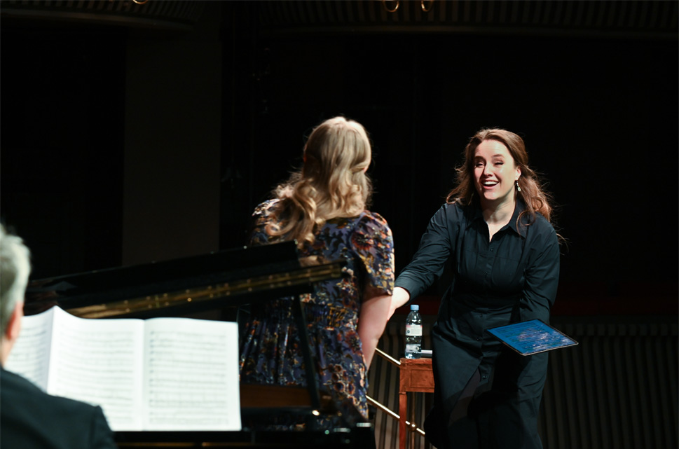 A female student shaking hands with Louise Alder, a women wearing a smart outfit, with brown hair, on stage.